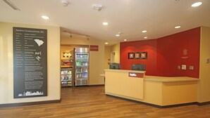 Zona de recepción con mostrador, refrigerador lleno de bebidas y un panel informativo sobre North Charleston, Carolina del Sur.