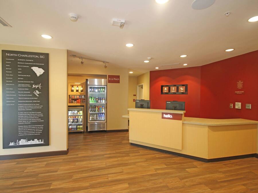 A reception area with a counter, a refrigerator stocked with beverages, and a wall-mounted information board detailing North Charleston, SC.