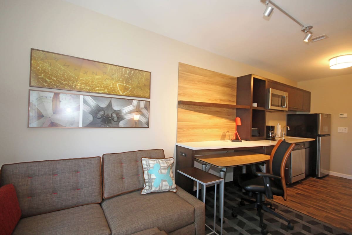Un espacio habitable compacto con kitchenette, comedor y un sofá con cojín.