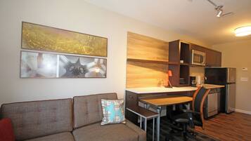 A compact living space with a kitchenette, a dining area, and a sofa with a cushion.