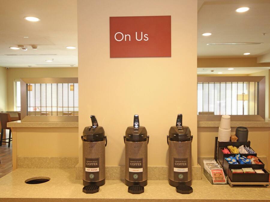 A coffee station with three coffee dispensers labeled 'Hot Water,' 'Decaf,' and 'Medium.' There is a sign above the dispensers that reads 'On Us.'