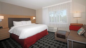 Una habitación de hotel con una cama grande, un sofá, una mesita y una ventana con cortinas traslúcidas.