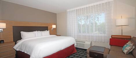 Una habitación de hotel con una cama grande, un sofá, una mesita y una ventana con cortinas traslúcidas.