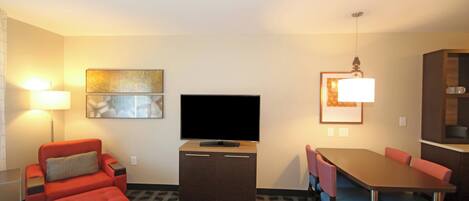 A hotel room with a flat-screen TV, a dining table with chairs, a red sofa, and a patterned floor.