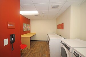 Un lavadero con una pared roja, un teléfono, una silla y dos lavadoras.