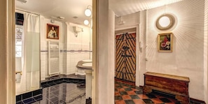 Un bagno con uno specchio grande, un lavandino e un water. Si nota una panca in legno e un elemento decorativo a parete.