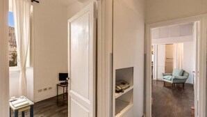A hallway with white walls, a wooden floor, and a door leading to a room with a blue chair. - Colosseo view Suite (Rome)
