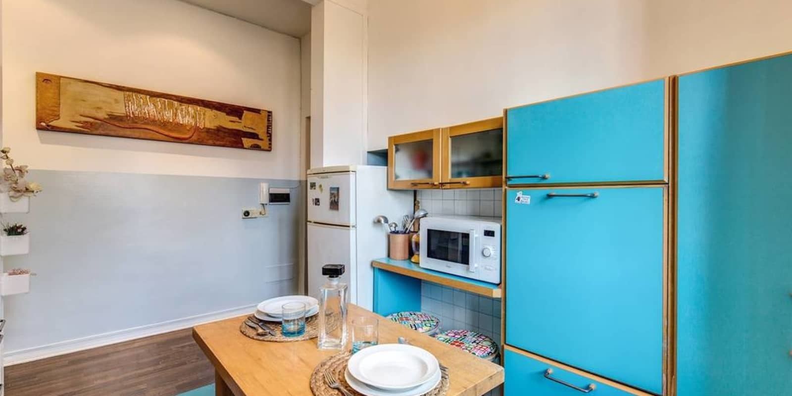 Eine Küche mit einem Holztisch, weißen Tellern, einer Mikrowelle und einem blauen Kühlschrank.