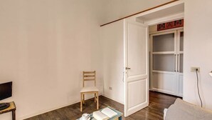 A room with a wooden chair, a table with a book and a cup, a TV, and a lamp. - Colosseo view Suite (Rome)