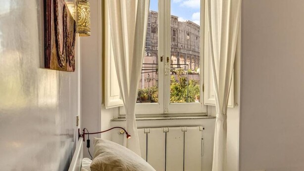 A room with a bed, a radiator, and a window with curtains. - Colosseo view Suite (Rome)