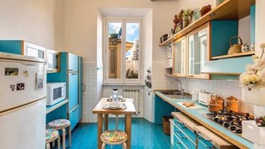 A compact kitchen with teal cabinets, a white refrigerator, and a blue tiled floor. - Colosseo view Suite (Rome)