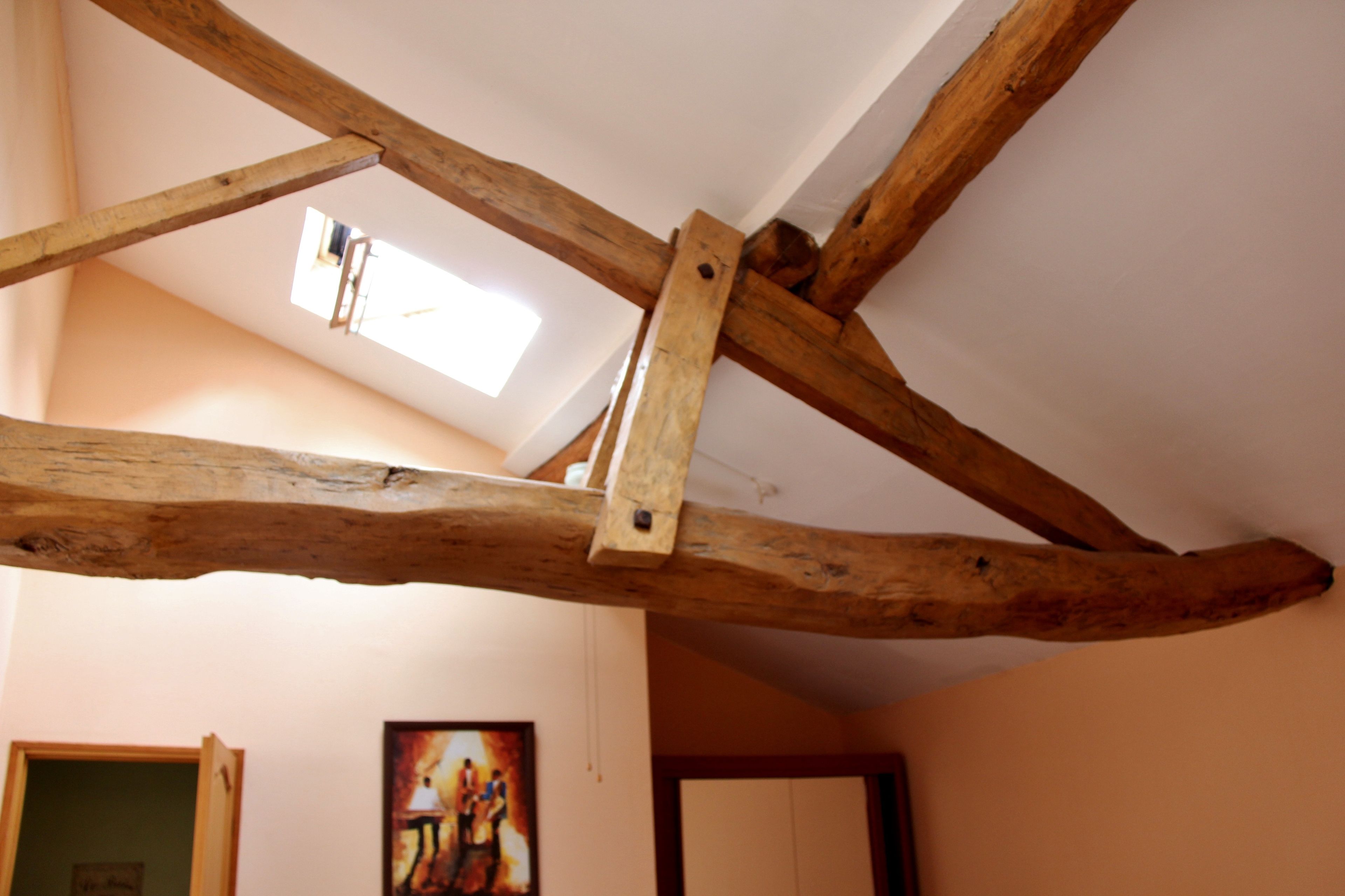 Una habitación con vigas de madera a la vista, un tragaluz y un cuadro en la pared.