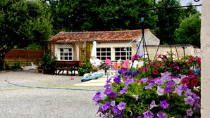 A rustic house with a tiled roof, a fenced yard, and a garden with purple flowers. - Chambre d'hôtes Les Cygnes Noirs (Aujac)
