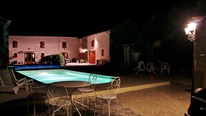 An outdoor swimming pool area with a table and chairs, a covered seating area, and a building in the background. - Chambre d'hôtes Les Cygnes Noirs (Aujac)