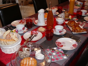 Et morgenbord dækket med tallerkener, bestik, brød, kager og drikkevarer.
