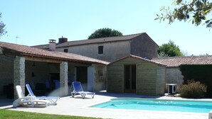 Un bâtiment à deux étages doté d’une piscine, de piliers en pierre et d’un patio couvert avec des chaises longues.