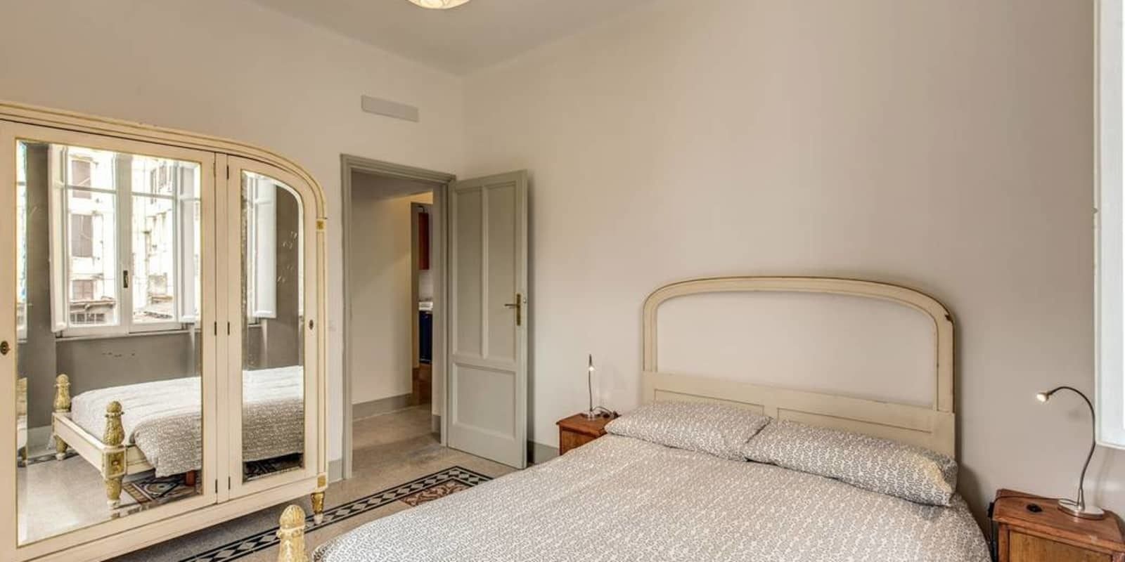 A bedroom with a bed, a wardrobe, a nightstand, and a mirror.
