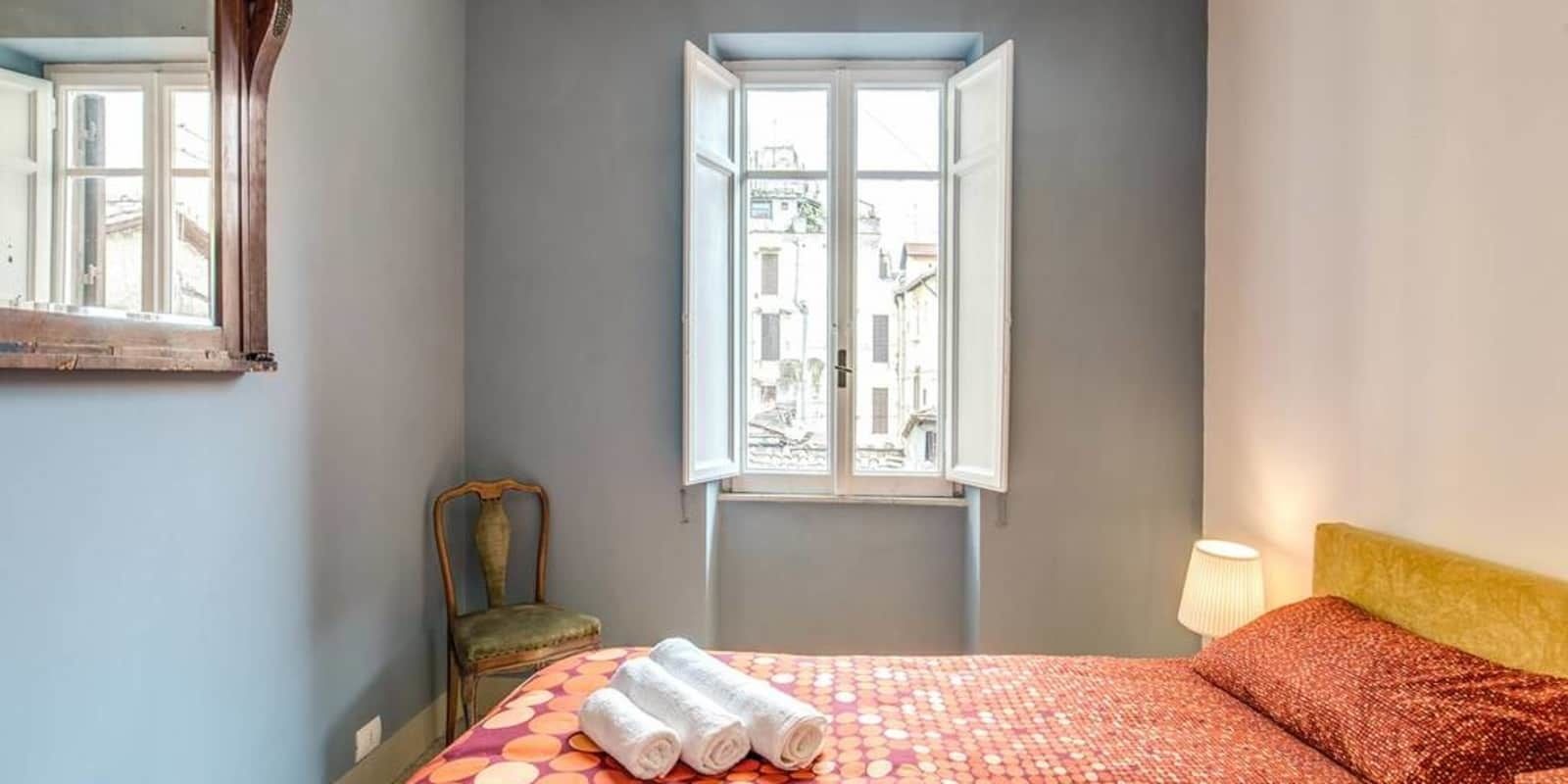 Une chambre à coucher avec un lit, une chaise, une fenêtre et une lampe.