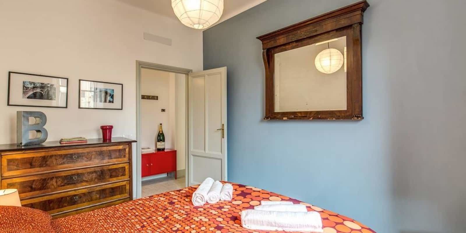 A bedroom with a bed, a dresser, a mirror, and a door leading to another room.
