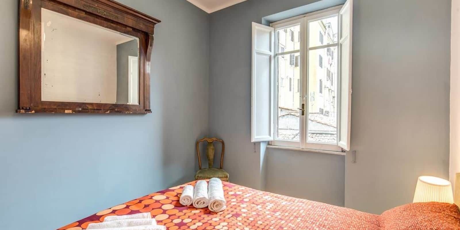 A bedroom with a bed, a window, a chair, and a mirror.