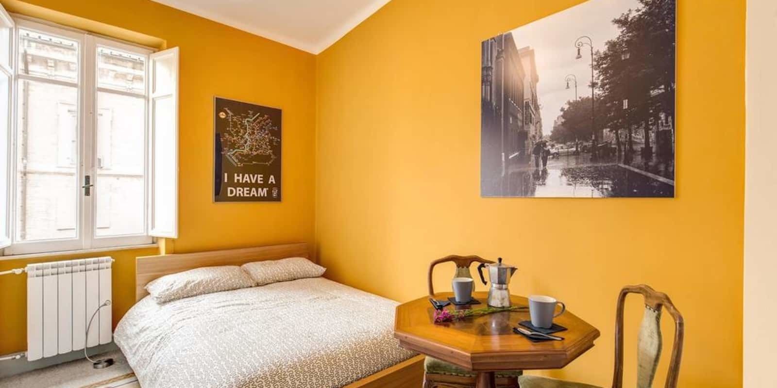 Een kamer met een bed, een tafel met een koffiezetapparaat en een poster aan de muur.