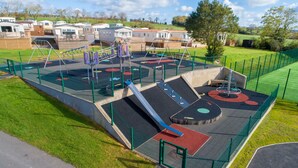 Ein Spielplatz mit unterschiedlicher Spielausstattung, umgeben von einem grünen Zaun und einer Rasenfläche.