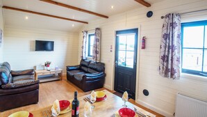 Ein gemütliches Wohnzimmer mit Holzbalkendecke, einer schwarzen Ledersofa, einem Esstisch gedeckt mit Tellern, Gläsern und Besteck sowie einer schwarzen Tür mit Fenster.