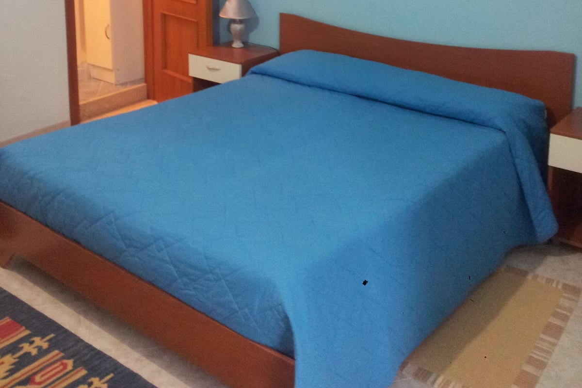 A bedroom with a bed, a nightstand, a lamp, a door leading to a bathroom, and a wall-mounted picture.