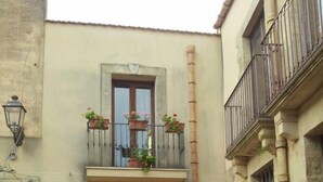 A courtyard with a stone wall, a wooden door, and a window with a balcony. - B&B Portagibli (Salemi)