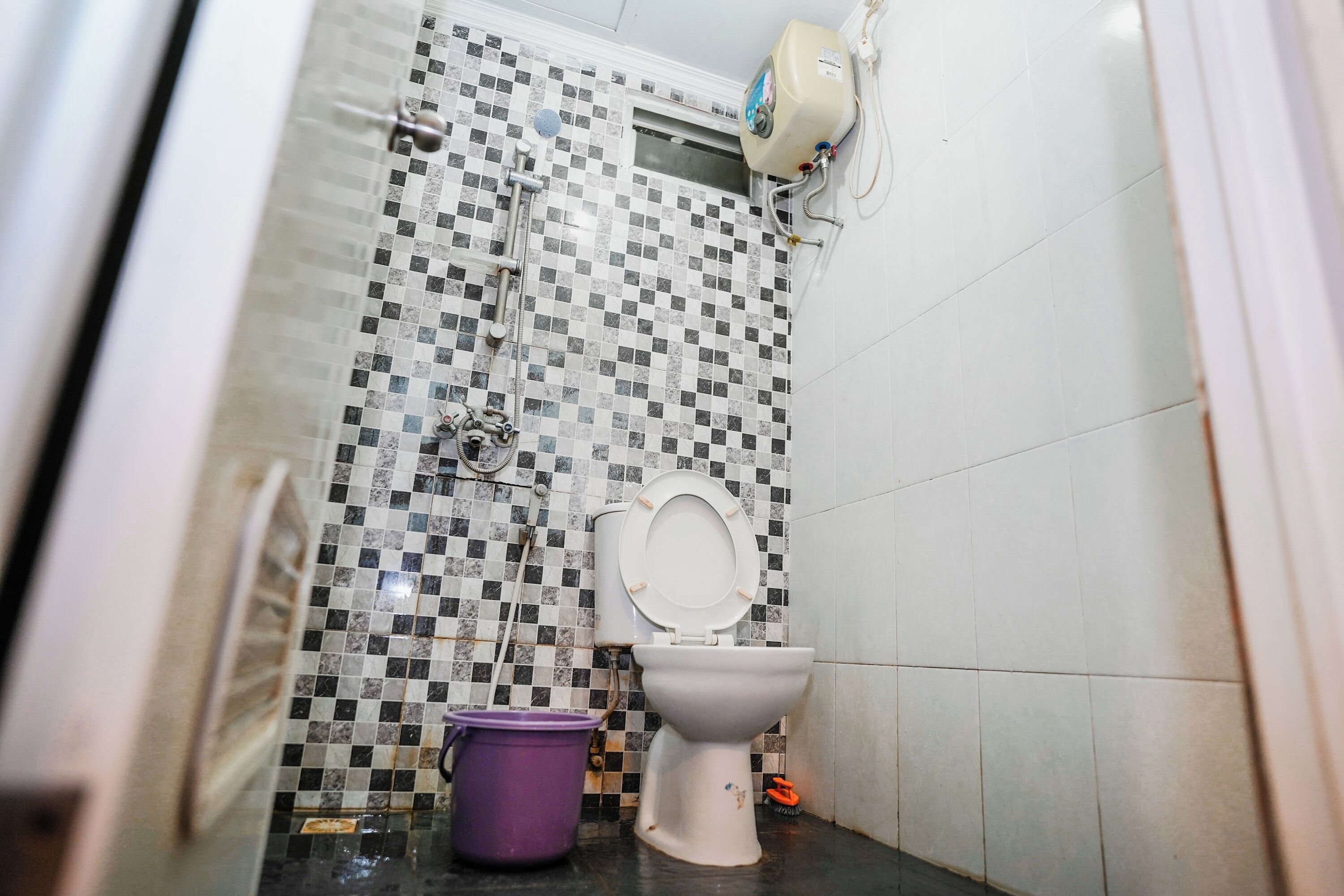 A small bathroom with a toilet, a shower, and a tiled wall.