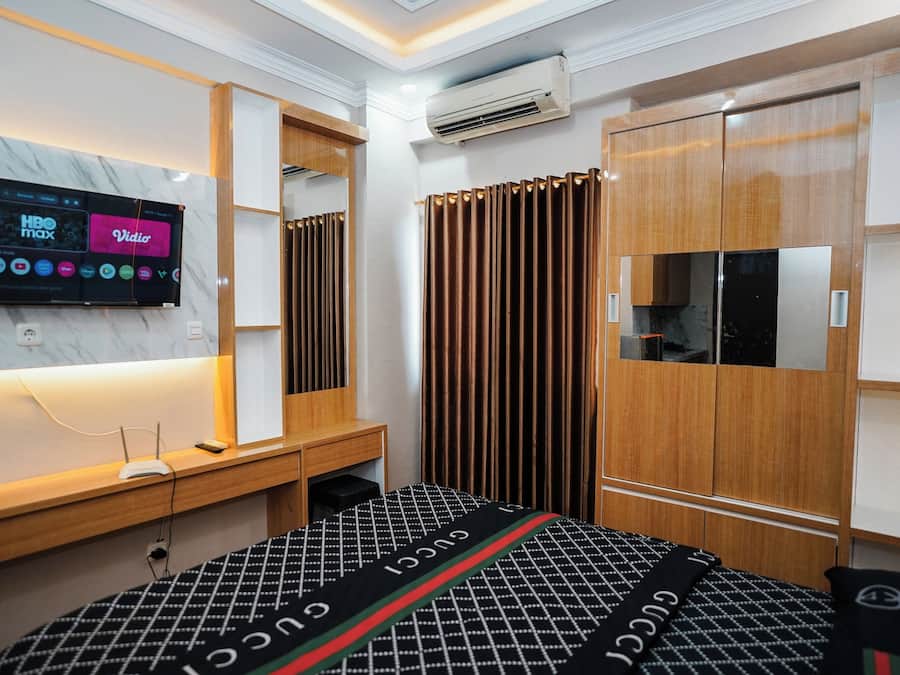 Une chambre à coucher moderne avec un téléviseur fixé au mur, une armoire en bois et un lit recouvert d’une couvre-lit à motifs.