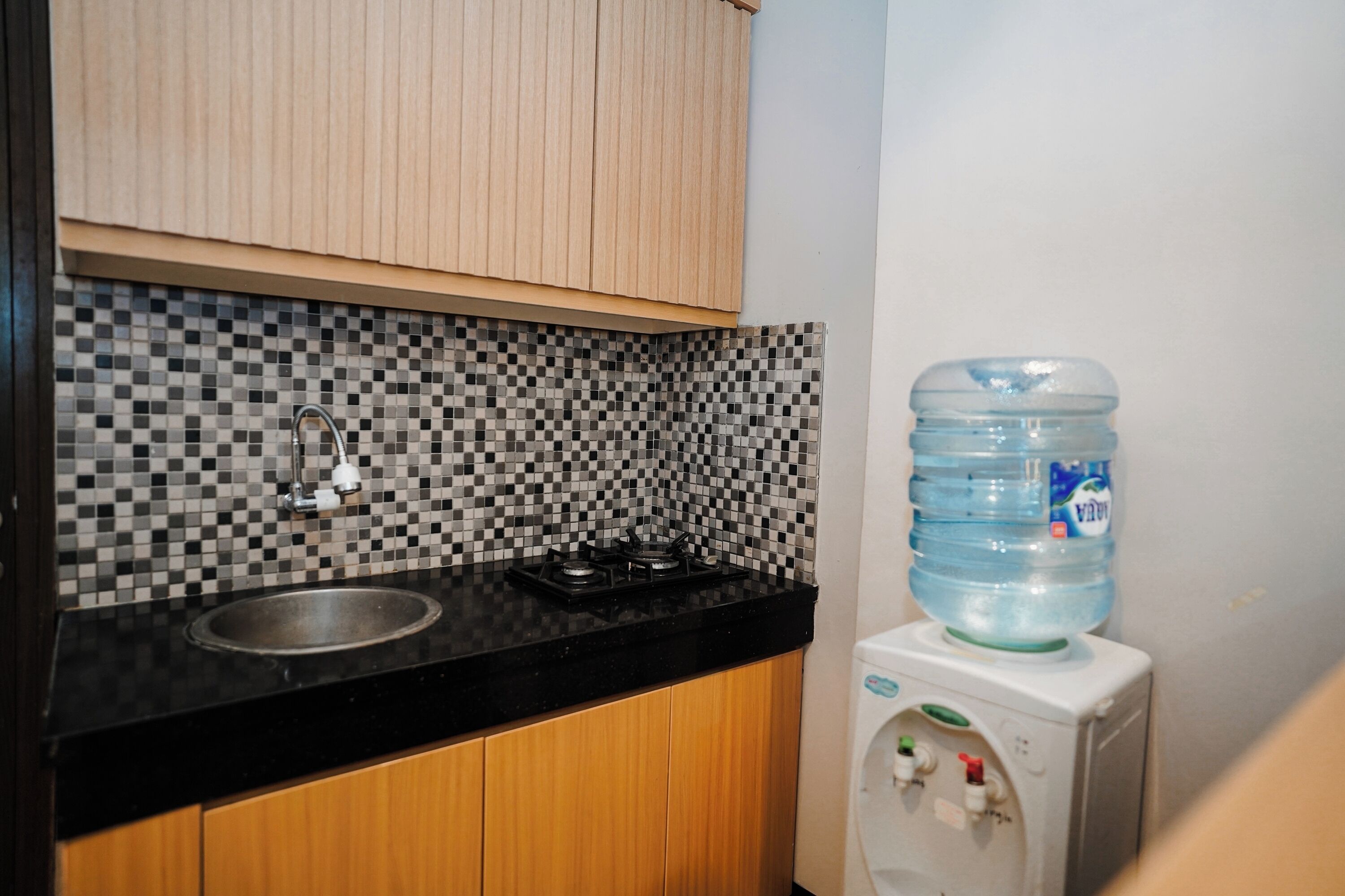 A kitchen with a black countertop, a sink, a gas stove, a tiled backsplash, wooden cabinets, and a water dispenser.