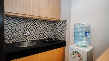 A kitchen with a black countertop, a sink, a gas stove, a tiled backsplash, wooden cabinets, and a water dispenser.