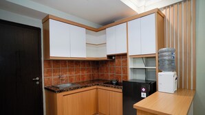 Una cocina compacta con armarios de madera, un refrigerador negro, un dispensador de agua y un salpicadero de azulejos.
