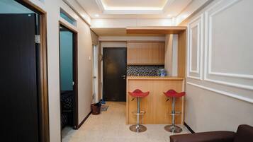 A hallway with a kitchen area, two red bar stools, and a brown chair.