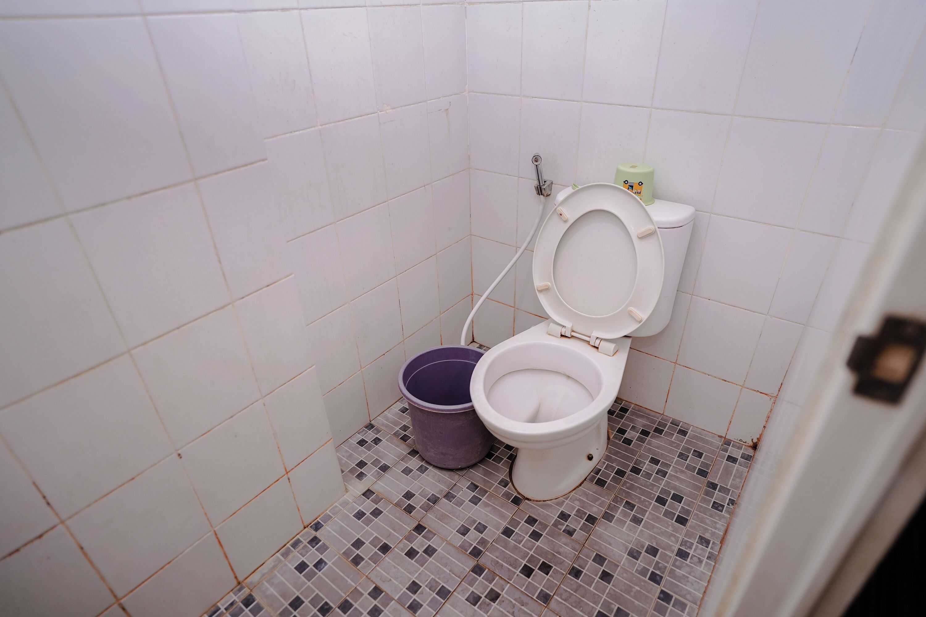 Ein kleines Badezimmer mit Toilette, Eimer und Fliesenboden.
