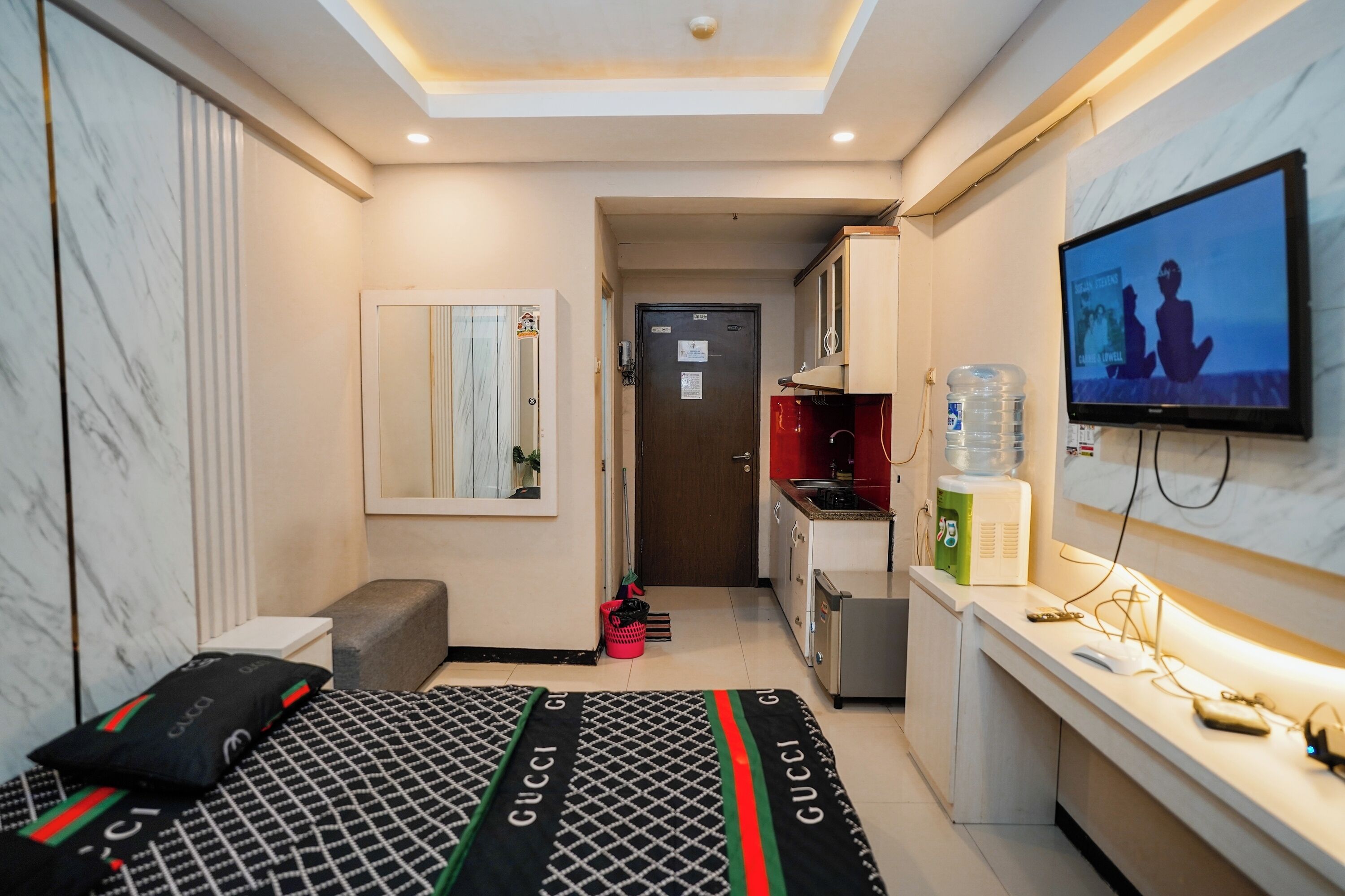A compact hotel room with a bed, a television, a small kitchenette, and a bathroom.