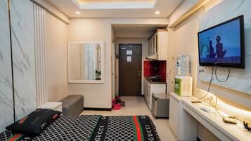 A compact hotel room with a bed, a television, a small kitchenette, and a bathroom.