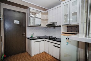 A compact kitchen with white cabinets, a black countertop, and a refrigerator with a cartoon character. - The Suites Metro Apartment - King Property (Bandung)