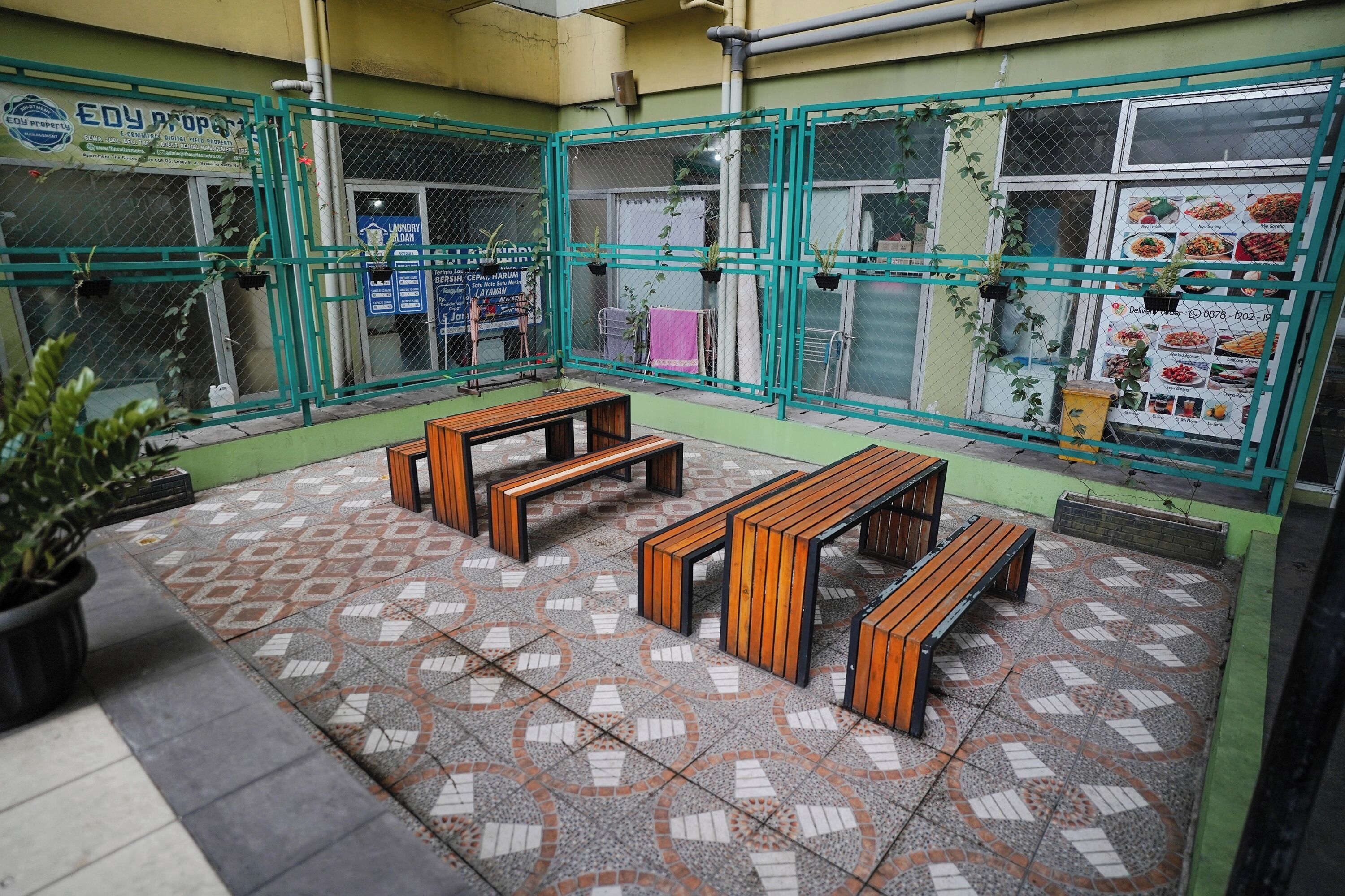 A courtyard with tiled flooring, wooden benches, and a green metal fence.