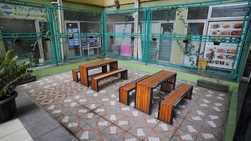 A courtyard with tiled flooring, wooden benches, and a green metal fence.