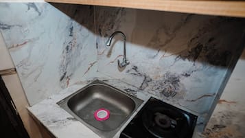 Uma cozinha com pia, torneira e um eletrodoméstico preto, possivelmente um fogão ou forno, sobre uma bancada de mármore.