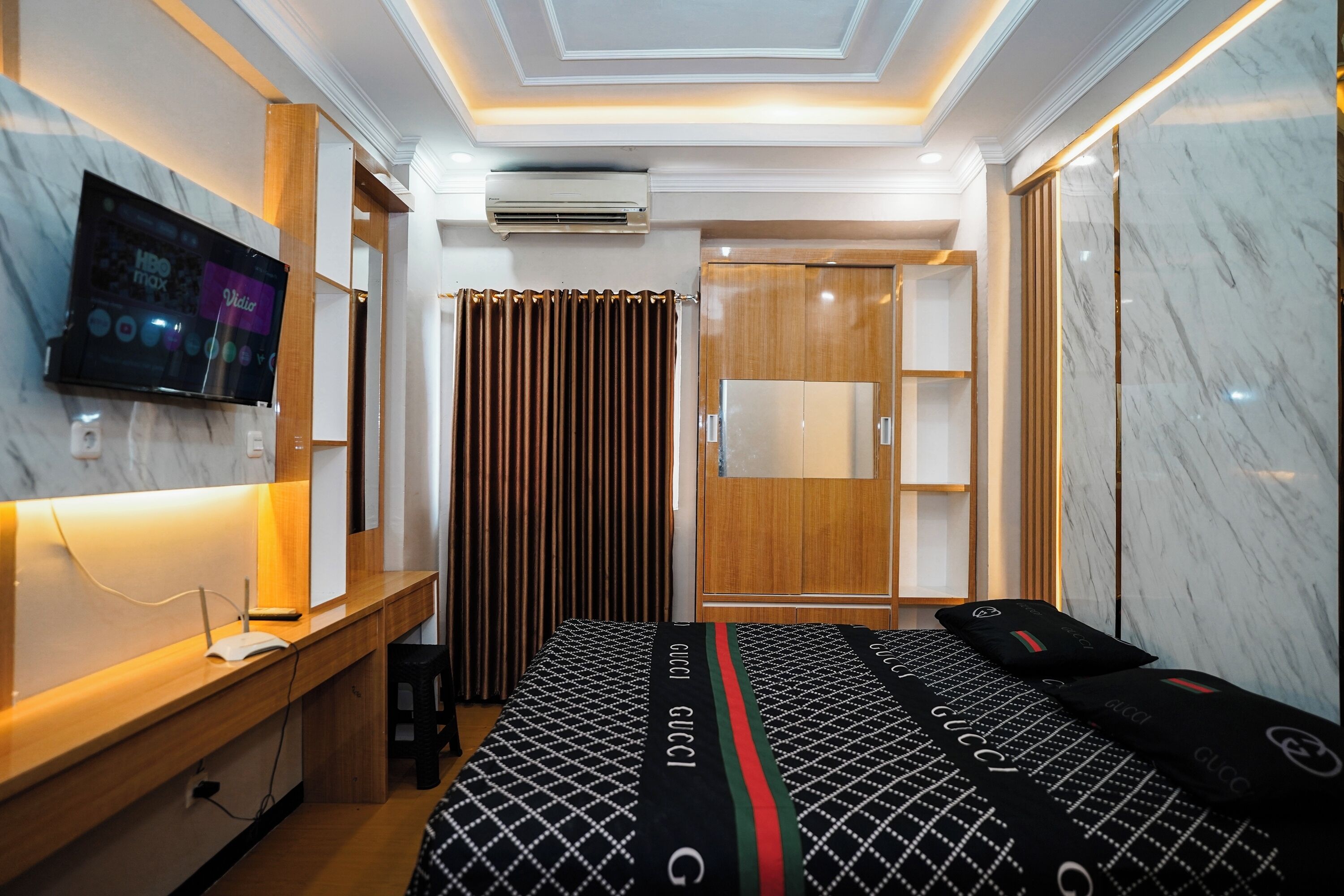 A hotel room with a bed, a desk, a television, an air conditioning unit, and a wardrobe.