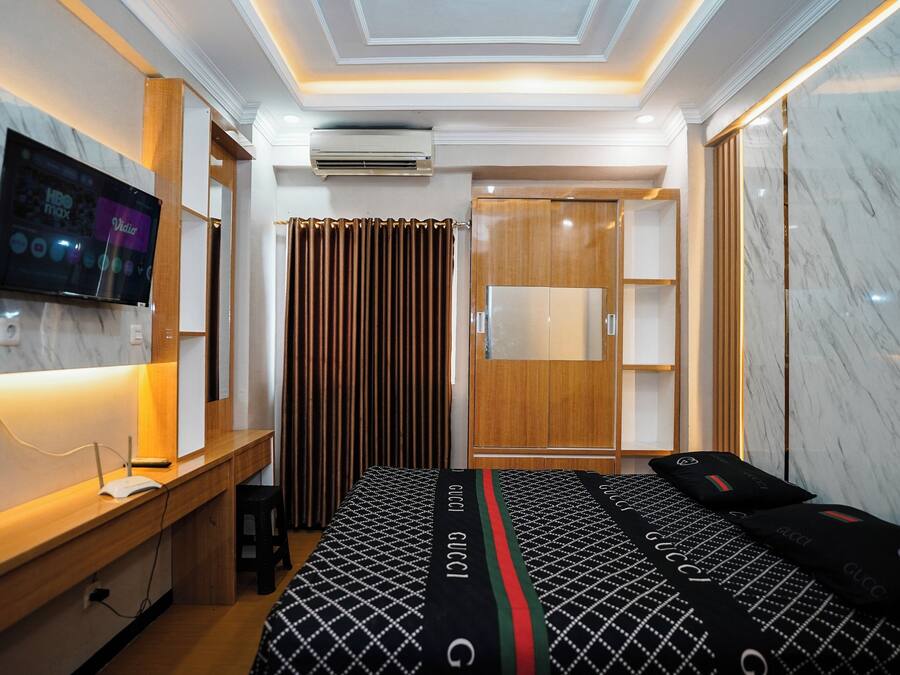 A hotel room with a bed, a desk, a television, an air conditioning unit, and a wardrobe.