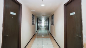 A long, narrow hallway with doors on both sides, each marked with a number. The floor is tiled, and the walls are plain. - The Suites Metro Apartment - King Property (Bandung)