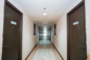 A long, narrow hallway with doors on both sides, each marked with a number. The floor is tiled, and the walls are plain.