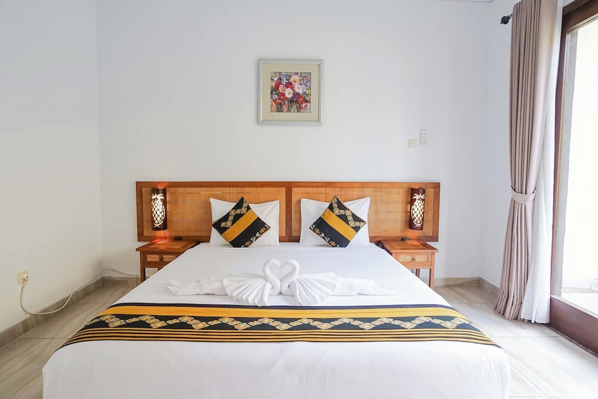 A neatly made bed with a decorative towel arrangement, a framed floral artwork on the wall, and a wooden headboard.