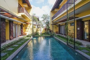 Un patio central con una piscina, rodeado de edificios amarillos con balcones y mesas al aire libre.