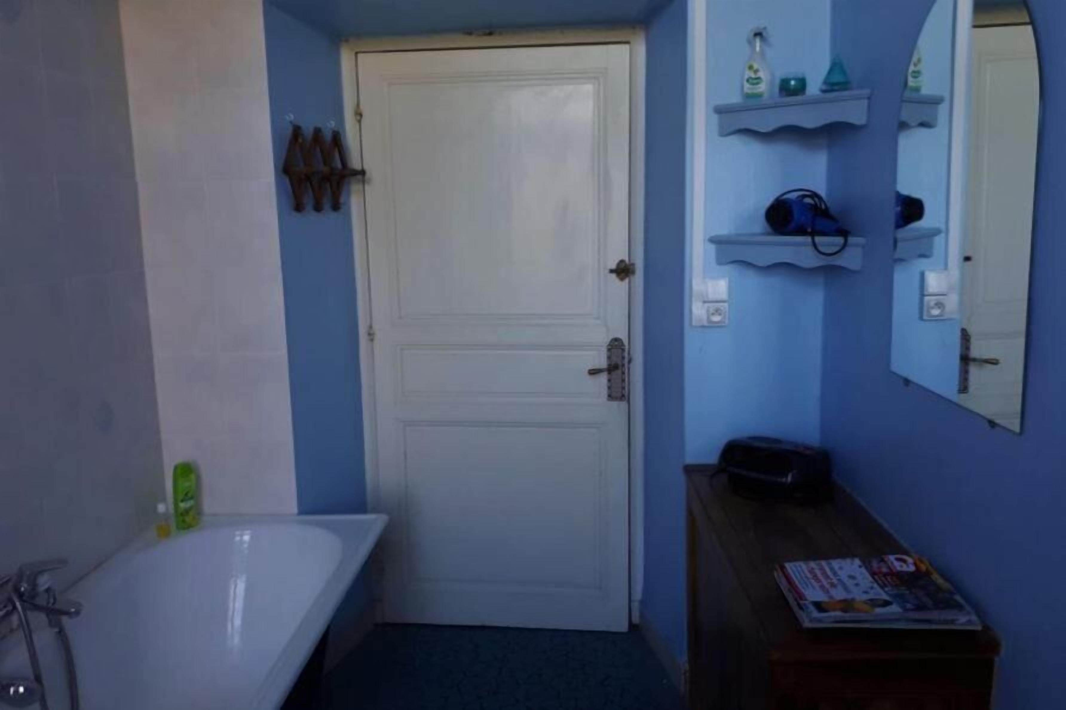 Een badkamer met een witte badkuip, een houten wastafelmeubel en een deur met een spiegel erboven.
