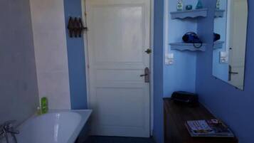 A bathroom with a white bathtub, a wooden vanity, and a door with a mirror above it.
